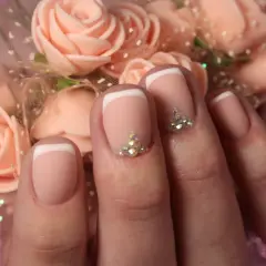 Elegancki french manicure z kryształkami, idealny na francuski swiateczny bal. Delikatne róże w tle dodają uroku.