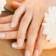 Delikatne dłonie z francuskim manicure, otoczone białymi kwiatami. Paznokcie wyglądają zdrowo, nie są suche.